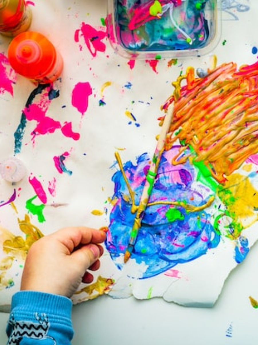 A child's hand reaches for vibrant paint colors amidst a happy mess.