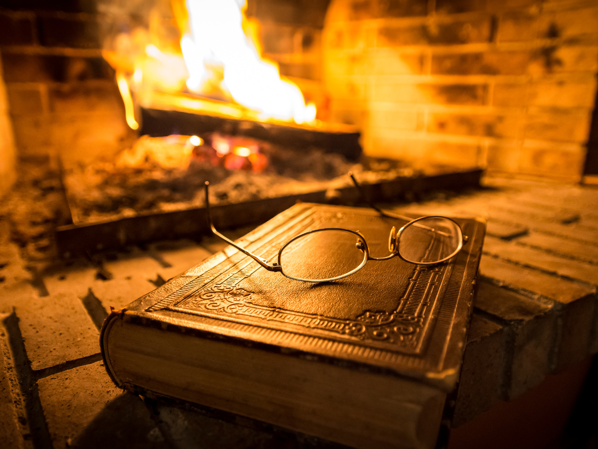 Glasses resting on top of a closed book in front of a fireplace