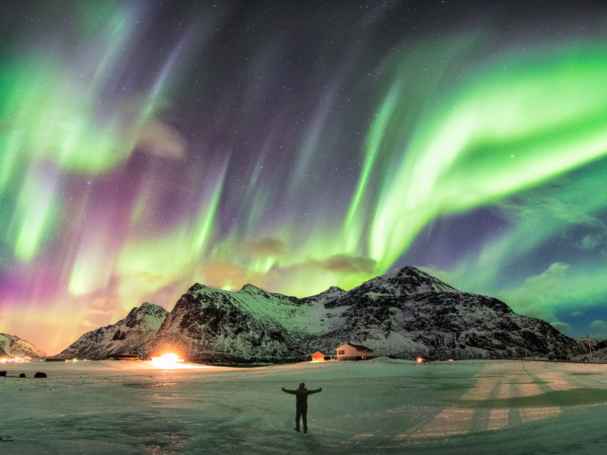 person standing in front of snowcapped mountain under blue, green, and purple northern lights