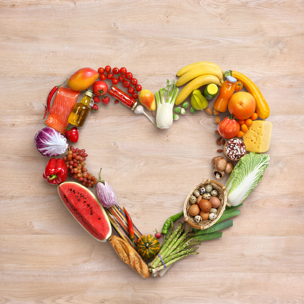 A rainbow of fruit and vegetable arranged in a heart shape on a light wooden background