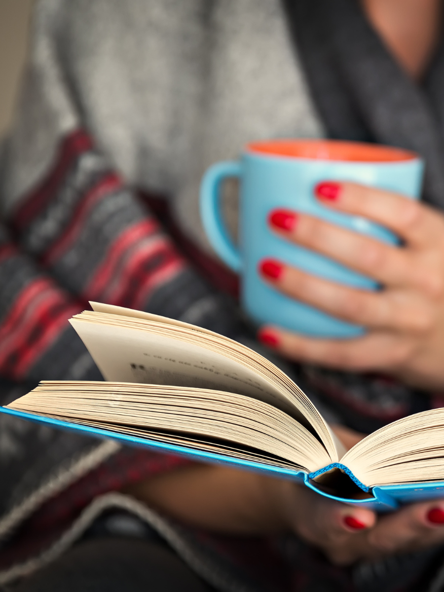 woman's hands holding book and mug