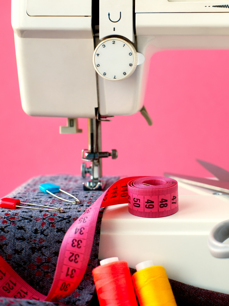 sewing machine with fabric under presser foot, and a tape measure, scissors, and spools of thread sitting nearby