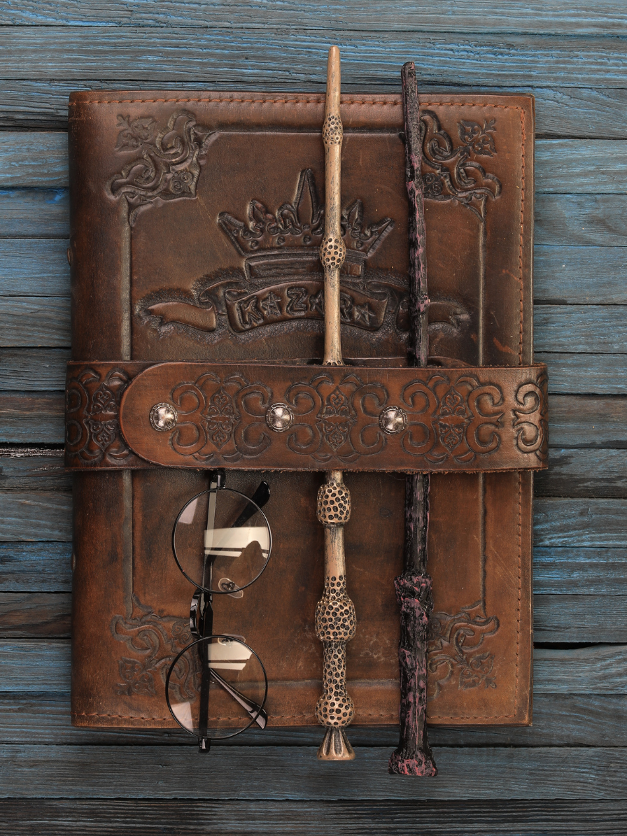 A weathered brown leather journal has a magic wand tucked into its cover.