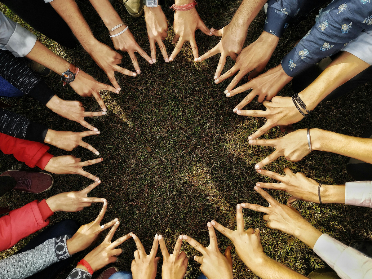 Many hands making the peace sign "V" gesture all in a circle.