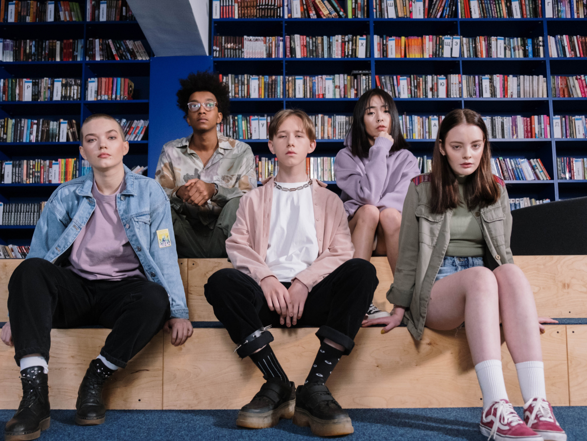 Several teens sitting in front of a bookshelf